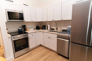 A modern kitchen with white cabinets, stainless steel appliances, a microwave, stove, dishwasher, and a refrigerator.