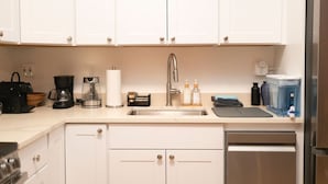 A kitchen with white cabinets, a stainless steel sink, a coffee maker, and a dishwasher.