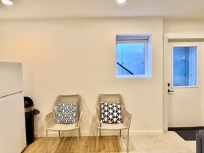 A room with two wicker chairs with patterned cushions, a small window, a door, and a trash bin.
