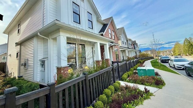 A row of two-story houses with a wooden fence, a sidewalk, and a street with cars.
