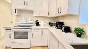 A modern kitchen with white cabinetry, a built-in oven, a microwave, a toaster, and a small potted plant.