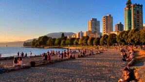 A beach with people, a body of water, and buildings in the background. - FIFA Stay 1BR| Steps to Seawall | Free Parking+AC (Vancouver)