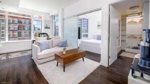 A modern living room with a sofa, coffee table, and a view of the city. - FIFA Stay 1BR| Steps to Seawall | Free Parking+AC (Vancouver)