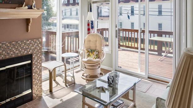 Una habitación con chimenea, una mesa de vidrio, un sillón acolchado y vistas a una terraza y edificios exteriores.