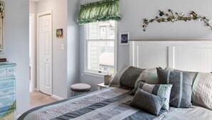 Un dormitorio con una cama grande, una ventana con persianas, un aparador y un adorno en la pared.