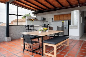Une cuisine avec un sol carrelé, une table en bois, des chaises noires, un banc et un réfrigérateur.