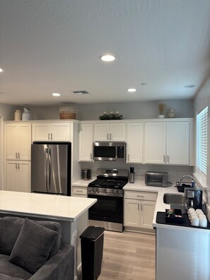 A modern kitchen with white cabinets, stainless steel appliances, a central island, and a built-in oven. - Sequoia Arcade House - New Build - Sleeps 10 (Visalia)