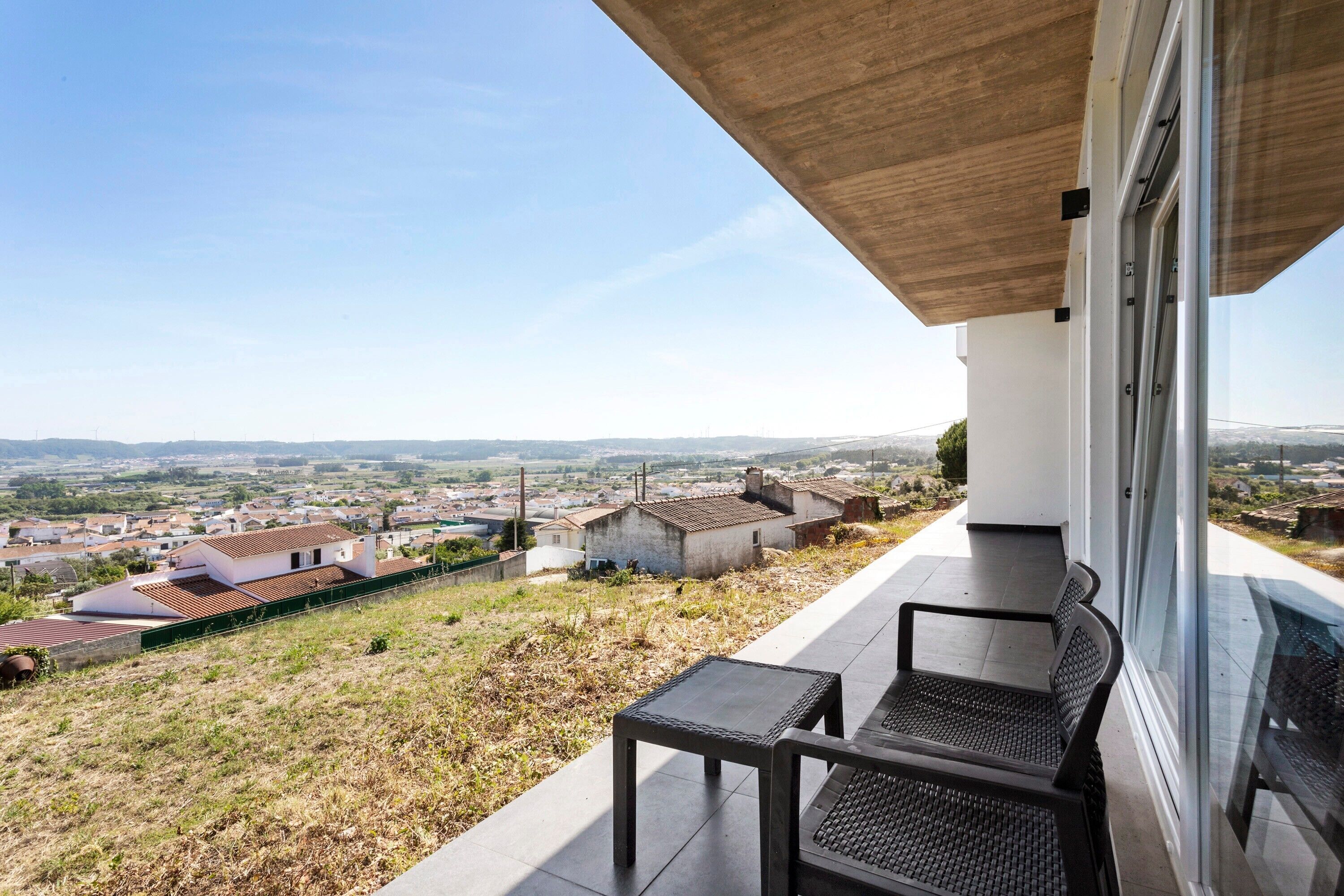 A balcony with a view of a town, a table, and two chairs.