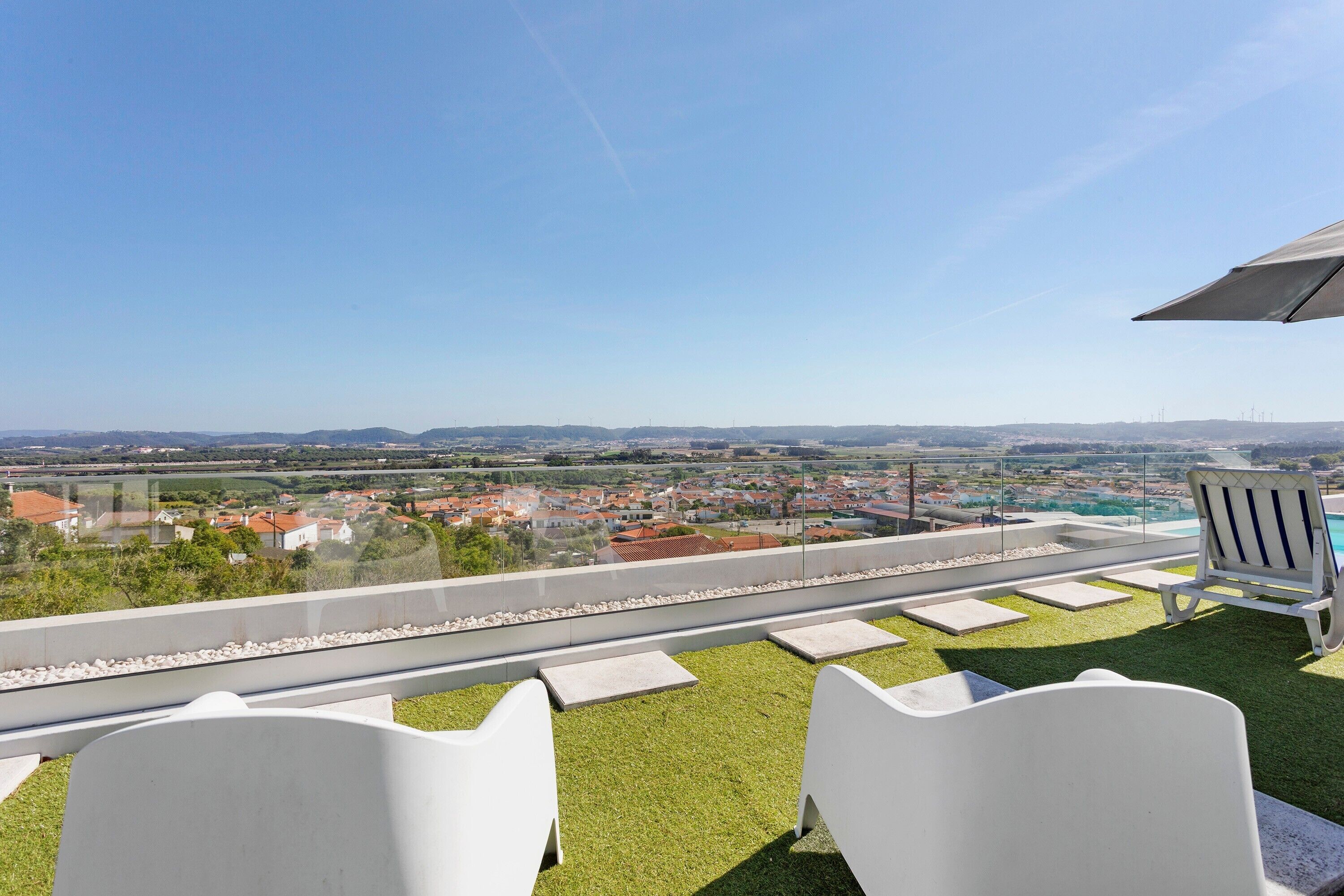 A rooftop terrace with a clear view of a town, a pool, and two white chairs.