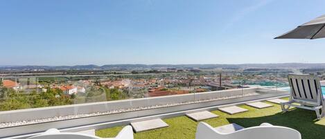 A rooftop terrace with a clear view of a town, a pool, and two white chairs.