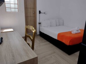 A room with a bed, a wooden chair, a table, and a window.