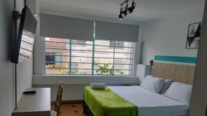 A hotel room with a bed, a desk, a chair, a window with a view, and a mounted television. - hotel boutique casa vecchia  (Cali)