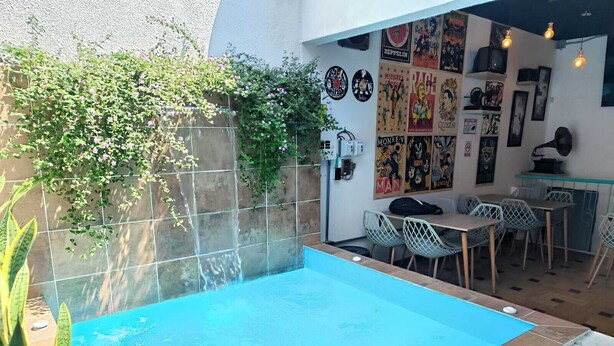 A swimming pool with a tiled deck, a dining area with chairs and a table, and a wall decorated with posters. - hotel boutique casa vecchia  (Cali)