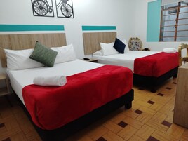 Habitación de hotel con dos camas, cada una con colcha roja y almohadas blancas, cabecero de madera y ventana con vistas.