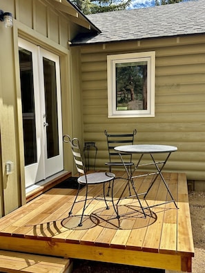 A wooden deck with a table and chairs, a sliding glass door, and a framed picture on the wall. - Crooked Pine Cottage- Close To RMNP Entrance (Estes Park)
