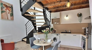 Eine moderne Küche mit Einbauwaschmaschine, einem Essbereich mit rundem Tisch und Stühlen sowie einer schwarzen Wendeltreppe.