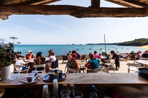 Ein Restaurant am Meer mit Terrassensitzplätzen und Blick auf das Meer, Tische mit Speisen und Getränken sowie eine Holzbalkendecke.