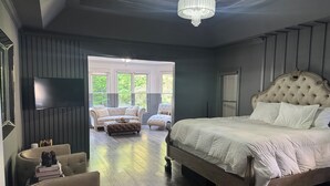 Ein Schlafzimmer mit einem großen Bett, einem Fernseher, einer Chandelüster und Blick ins Freie.