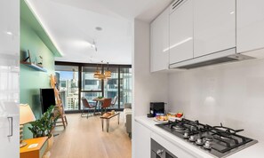 A modern kitchen with a gas stove, a dining area with a table and chairs, and a view of the city through large windows. - Sky Tower Luxe Retreat Pool & Gym (Brisbane City)