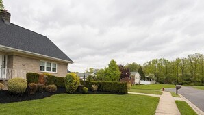 A residential street with a well-maintained lawn, a sidewalk, and a house with a brick facade and a dark roof. - North Brunswick 2BR | Easy Access to NYC & Rutgers (North Brunswick Township)