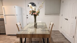 A dining area with a wooden table, chairs, a vase with flowers, a refrigerator, and a door with a window. - North Brunswick 2BR | Easy Access to NYC & Rutgers (North Brunswick Township)
