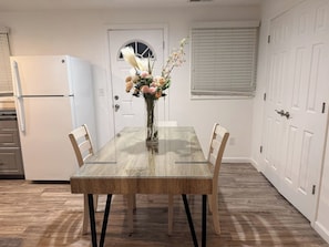 A dining table with chairs, a vase with flowers, a white refrigerator, and a door with a window.