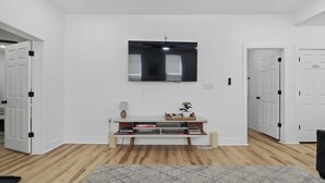 Een moderne woonkamer met een flatscreen televisie aan de wand, een houten vloer en een witte deur aan de linkerkant.