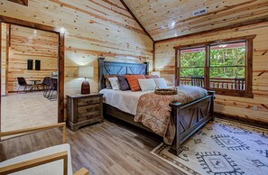 A wooden cabin bedroom with a bed, dresser, and a view of the outdoors.