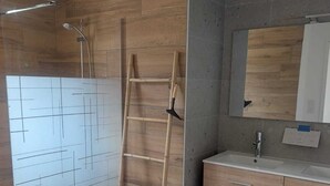 Ein Badezimmer mit Dusche, einer Holzleiter, einem Waschbecken mit Spiegel und einer gefliesten Wand.
