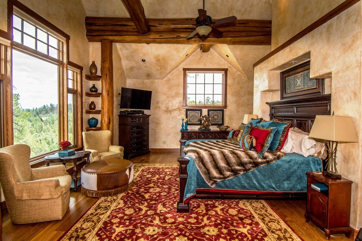 A spacious bedroom with a large bed, a sitting area with a chair and ottoman, a television, and a fireplace.