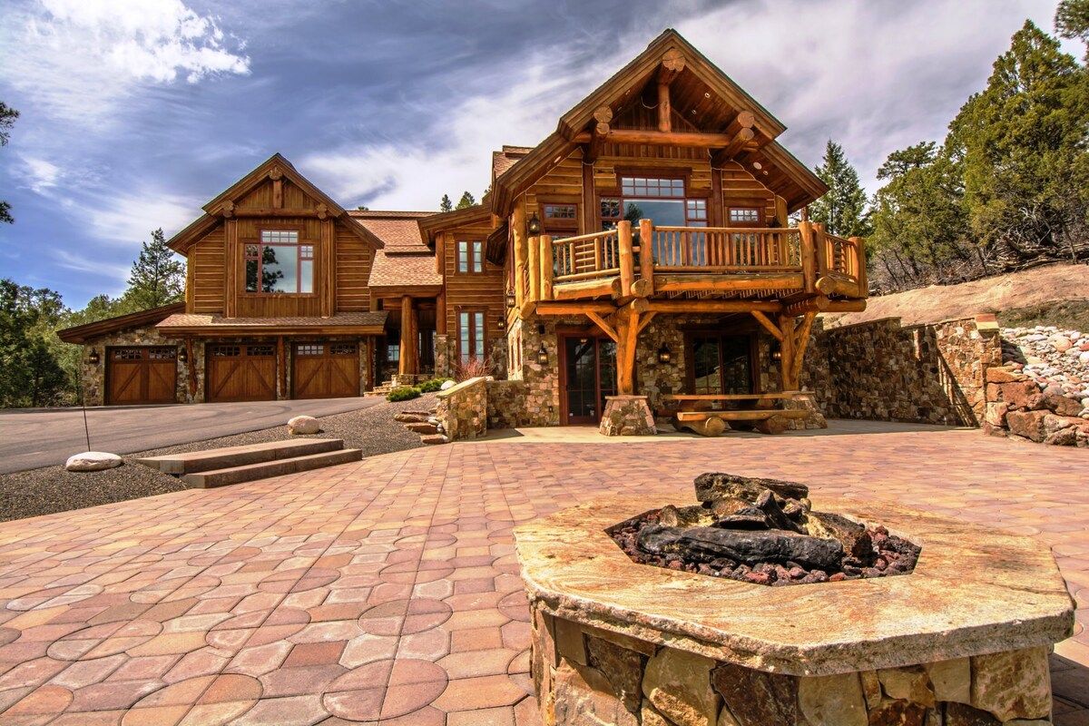 Una casa de madera grande con chimenea de piedra, un porche cubierto y un muro de piedra.