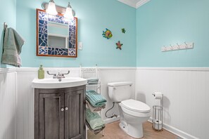 A bathroom with a white toilet, a sink with a mirror, and a towel rack. - Mermaid Hideaway | Quaint & Affordable Tropical Getaway! (Cheriton)
