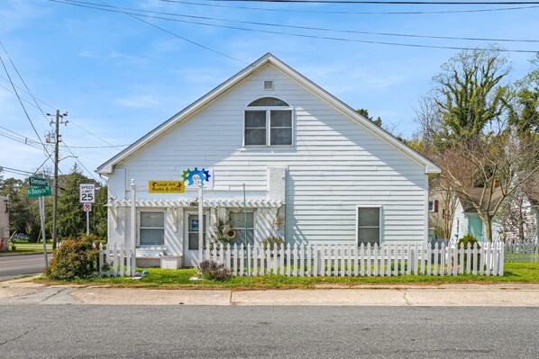 A white building with a white picket fence, a sign for 'Local Art Books & Gifts,' and a speed limit sign of 25 mph. - Mermaid Hideaway | Quaint & Affordable Tropical Getaway! (Cheriton)