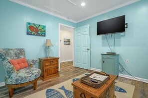 A living room with a teal wall, a television mounted above a cabinet, a chair with a cushion, a lamp, and a rug with a fish pattern.