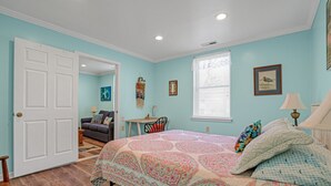 Un dormitorio con cama, una silla, una mesa y una puerta que da a otra habitación.