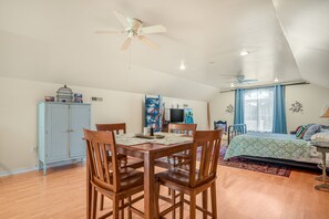 A room with a dining table, chairs, a bed, a TV, and a ceiling fan.