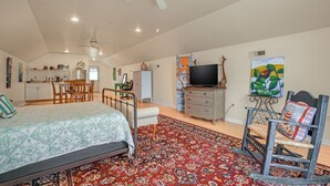 Une chambre à coucher avec un lit, un fauteuil à bascule, une télévision et, au fond, une cuisine.