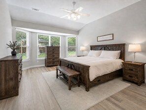 Ein Schlafzimmer mit einem hölzernen Bett, zwei Nachttischen, einem Schminktisch, einer Kommode, einer Bank und einem Deckenventilator.