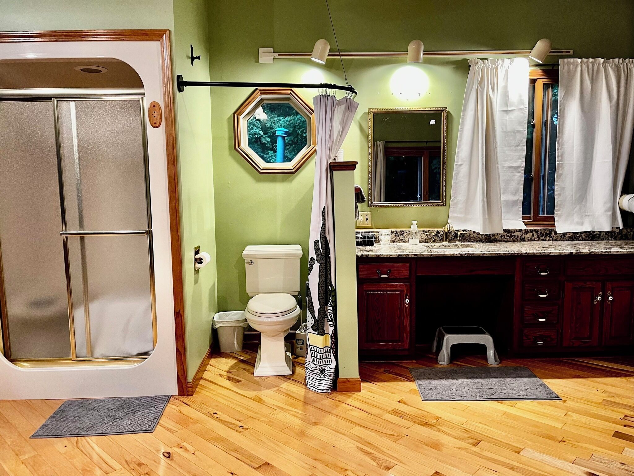 A bathroom with a toilet, a shower, a vanity with a mirror, and a window with a view of trees.
