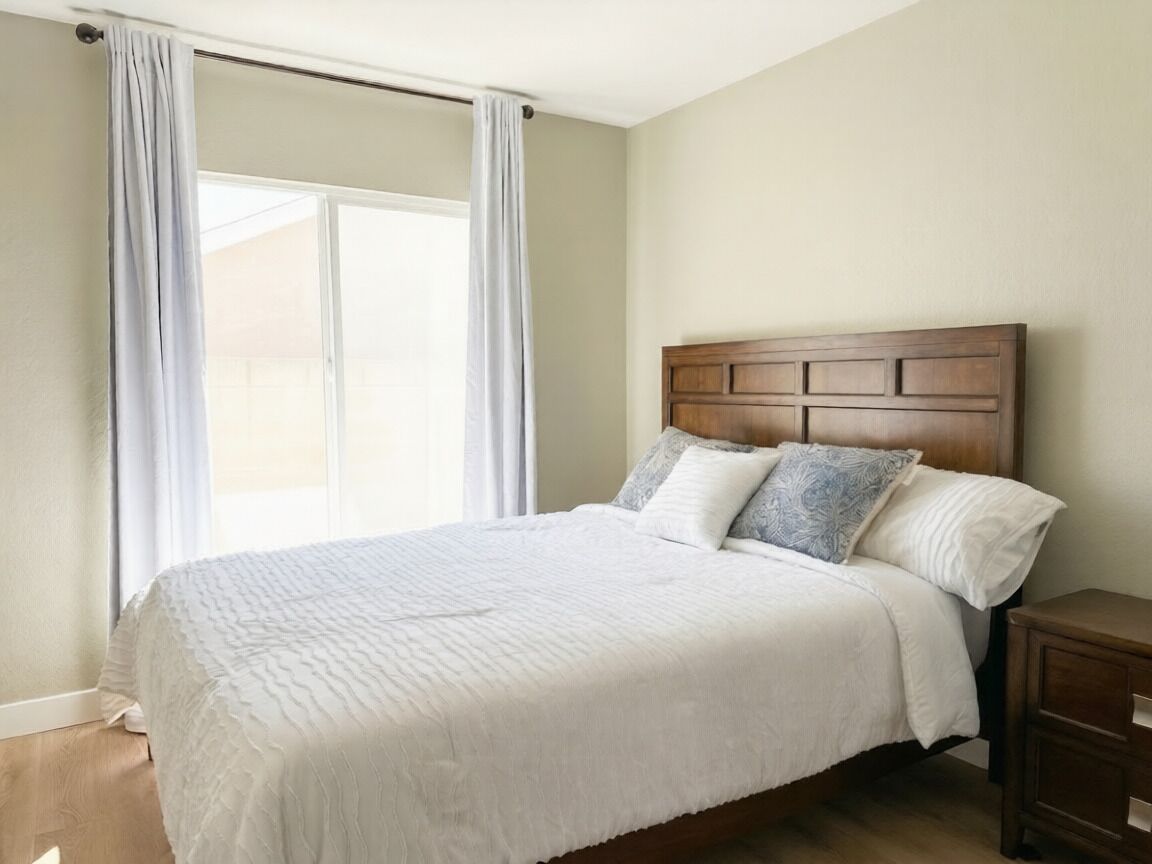 A bedroom with a wooden headboard, a white bedspread, and a nightstand.