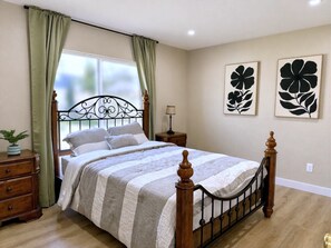 Ein Schlafzimmer mit Bett, Holzkommode, Nachttisch, Lampe und zwei Wandbildern.