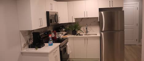 Una cocina moderna con armarios blancos, electrodomésticos de acero inoxidable, microondas y refrigerador.