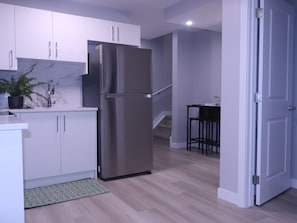 Eine moderne Küche mit weißen Schränken, einem Edelstahlkühlschrank, einer Marmor-Spritzschutzwand und einem Holzboden.