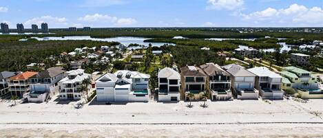 Un quartier résidentiel situé sur la côte, avec des propriétés donnant sur la plage, une végétation luxuriante et une vue lointaine sur les gratte-ciel de la ville.