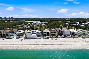 A coastal residential area with beachfront properties, dense vegetation, and a distant city skyline. - Gulf Breeze Retreat | Walk to Beach + Bay Views (Bonita Springs)