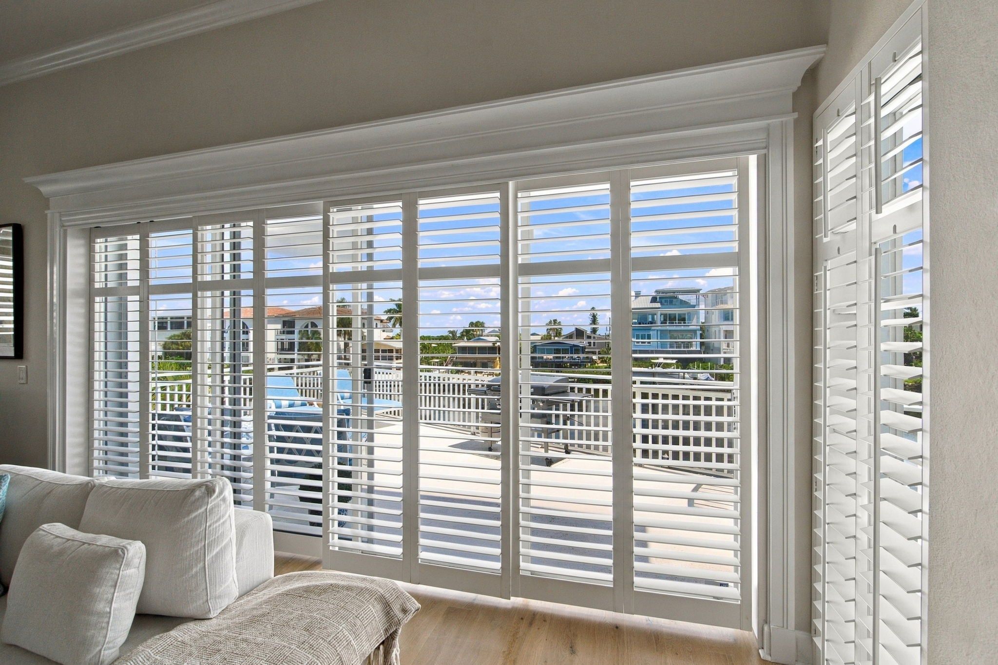 A room with a large window with white blinds, a sofa, and a view of a pool and buildings.