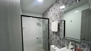Un baño con cabina de ducha de vidrio, inodoro, lavamanos con espejo y azulejos estampados.