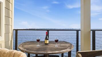 A wooden table with two wine glasses and a bottle on a balcony overlooking a body of water.