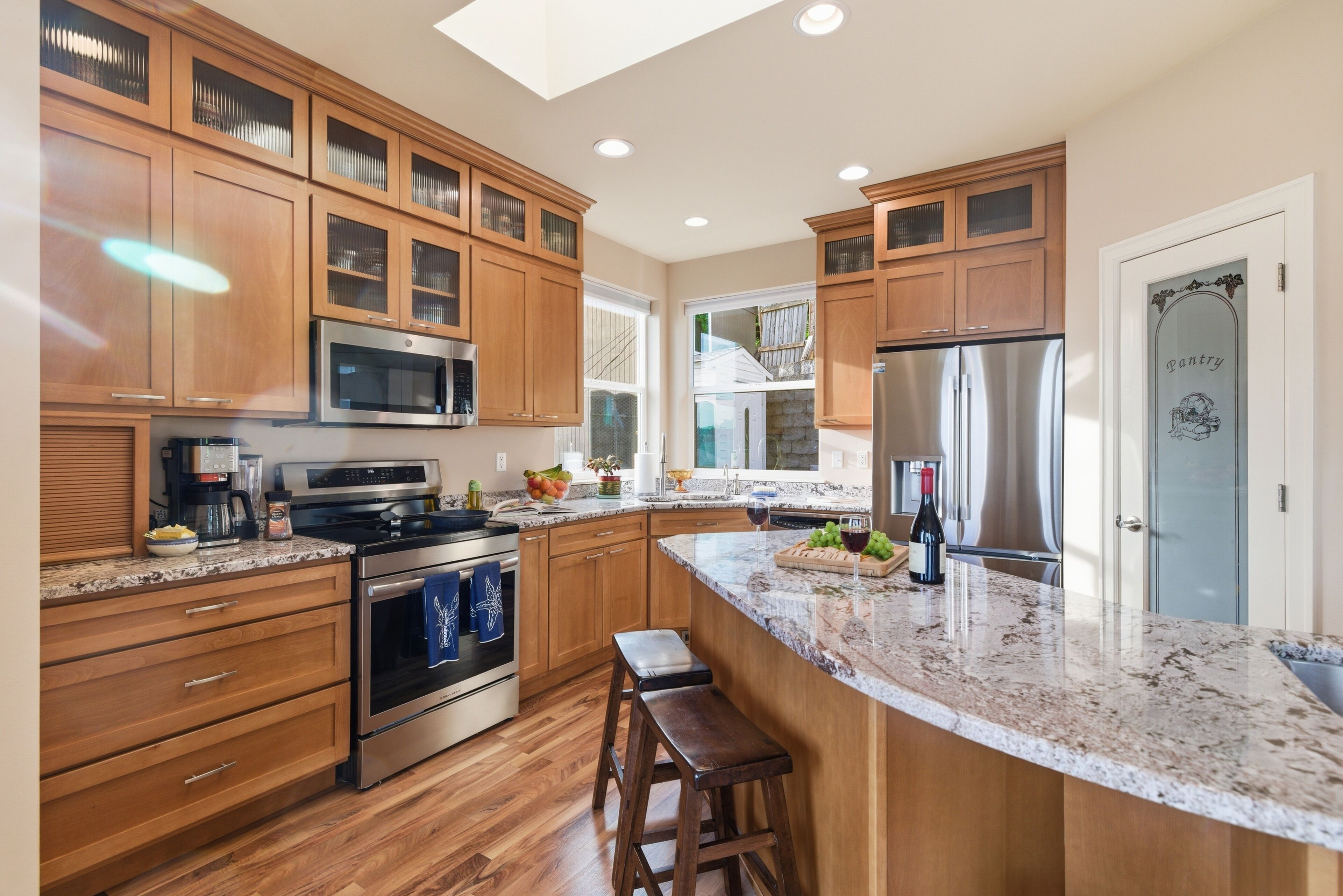 A modern kitchen with wooden cabinets, a granite countertop, stainless steel appliances, and a large island with stools.