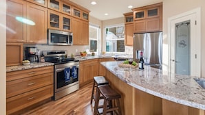 A modern kitchen with wooden cabinets, a granite countertop, stainless steel appliances, and a large island with stools.